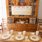 A Thanksgiving table setting featuring the Turkey & Gourds: Thanksgiving Table for 16 set with heavy-duty paper plates, gold chargers, and cups, with a happy fall banner hung on the hutch behind the table.