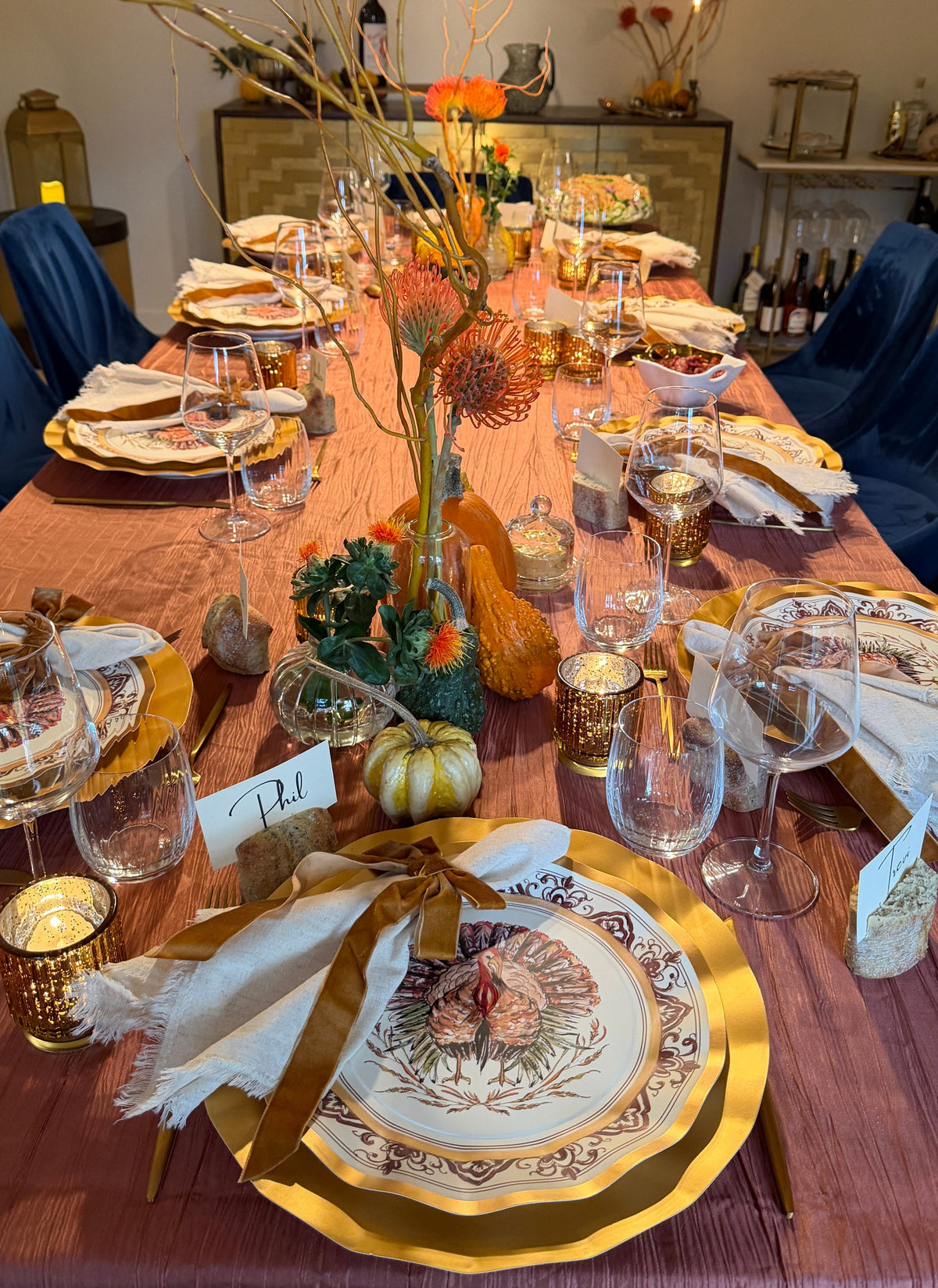 A Sophistiplate LLC Turkey & Gourds: Thanksgiving Table for 16 set on a mauve tablecloth with velvet ribbons, gourds, and floral centerpieces.
