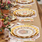 Create a warm autumn tablescape with the Turkey & Gourds Table Setting Bundle from Sophistiplate LLC, featuring designer disposable plates with gold trim, floral-patterned napkins, elegant gold cutlery, and charming autumn floral centerpieces—all beautifully set atop a rustic burlap and plaid tablecloth.