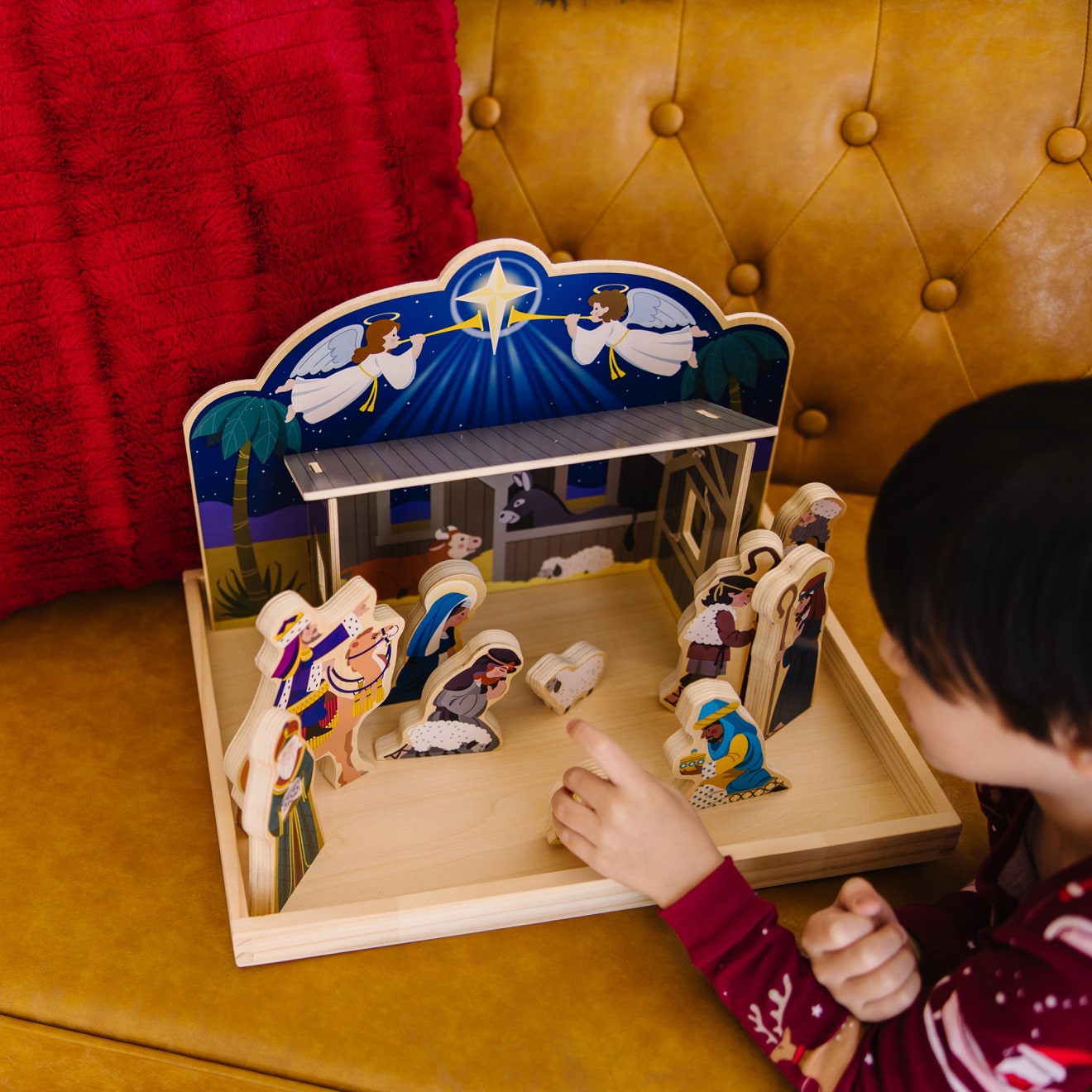 A kid playing with the Melissa & Doug Classic Wooden Christmas Nativity Set With 4-Piece Stable and 11 Wooden Figures