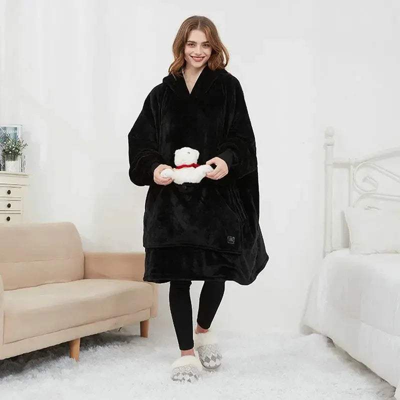 Woman wearing a black Oversized Heatable Hoodie holding a white teddy bear in a bedroom setting.