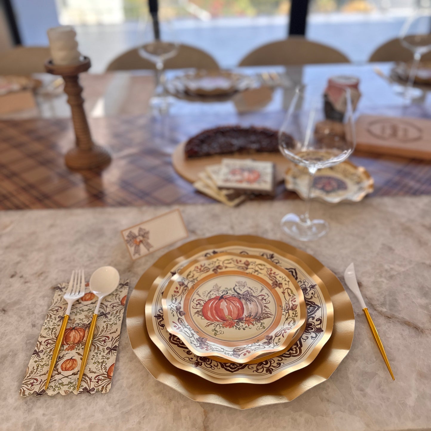 Sophistiplate Turkey & Gourds Table Setting featuring a gold-rimmed designer paper plate with a pumpkin illustration, gold-handled flatware, and a matching patterned napkin on a marble table.